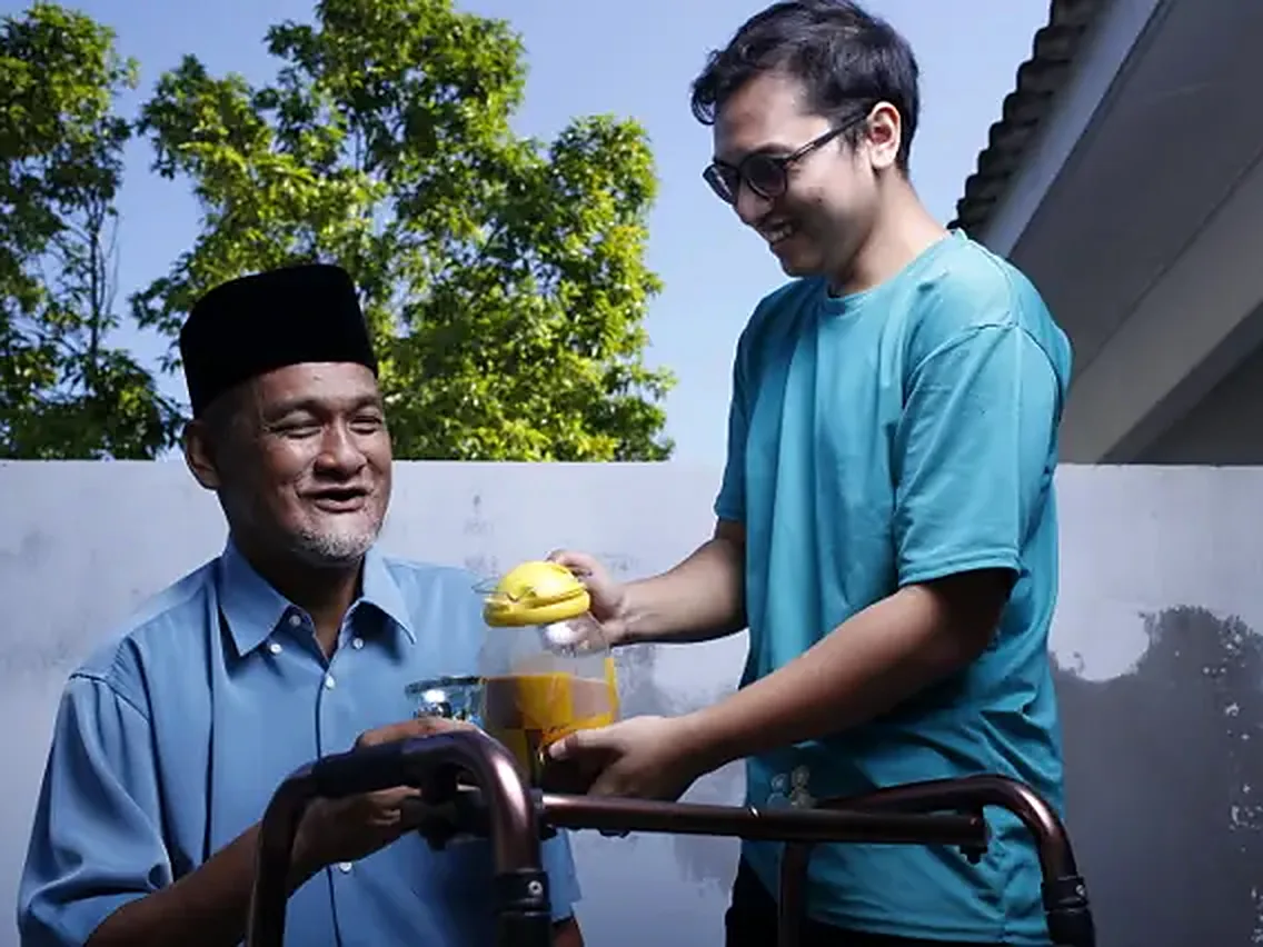 A senior and his carer sharing a drink outdoors